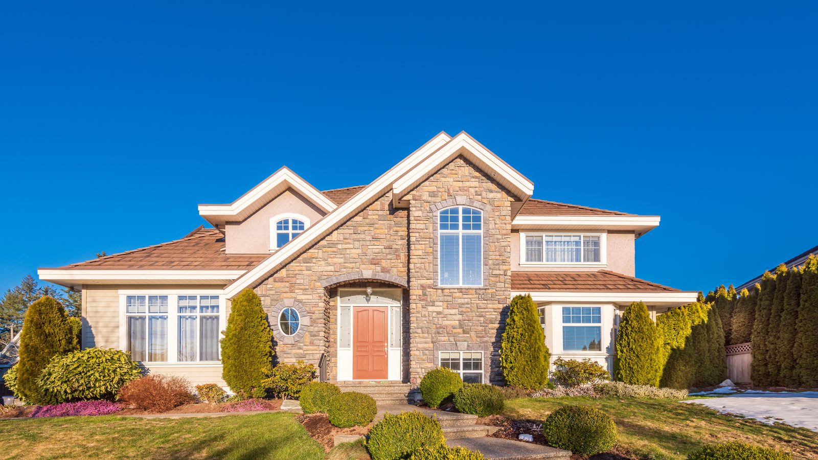 A two-story family home with a stone facade under a blue sky
